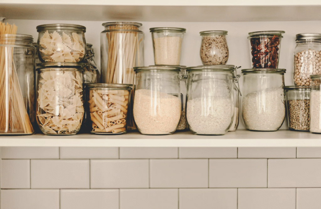 Glass jars filled with pasta, grains, and spices organized on a shelf in a tidy pantry, showcasing effective storage solutions for small kitchen spaces in urban apartments.