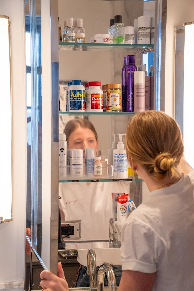 Woman organizing a bathroom cabinet with various skincare and medication products, illustrating the importance of structured spaces for adults with ADHD in NYC.