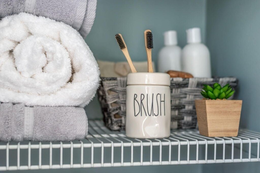 Bathroom under-sink organization New York, NY: neatly folded towels, toothbrushes in holder, and a potted succulent on a shelf to save space.
