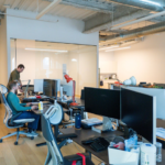 An open plan office with desks and clutter magnets that create a busy workspace environment in a modern New York, NY office.
