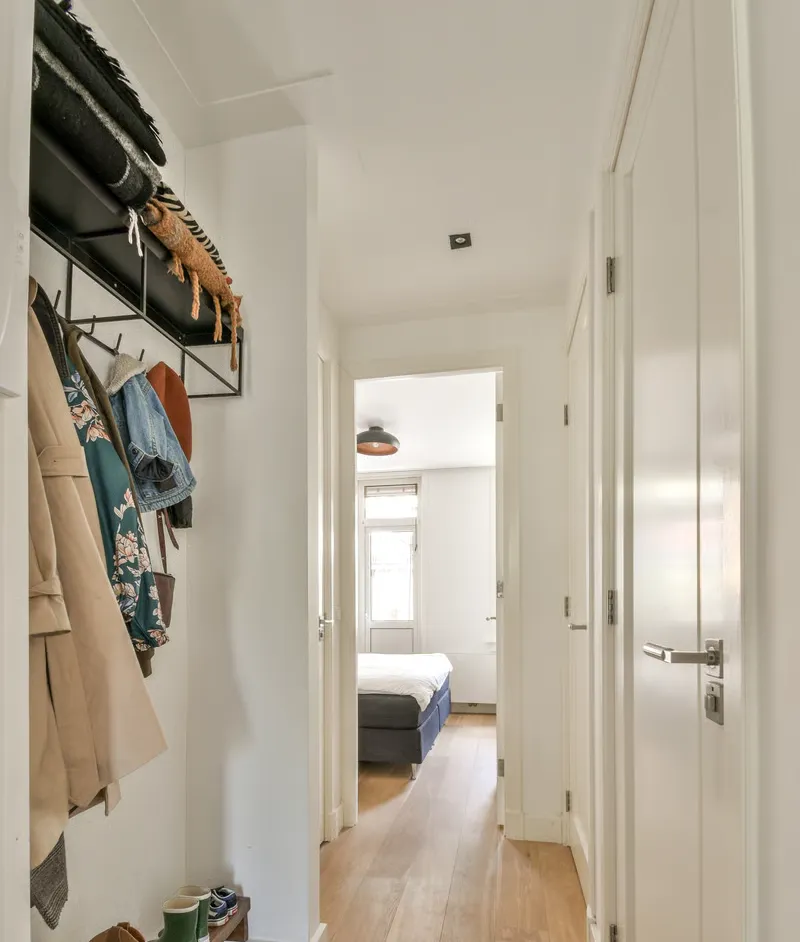 A hallway with a wall-mounted rack holding coats and shoes to ensure your home stays organized in this bright modern space