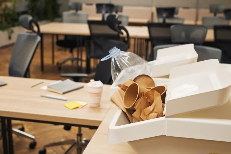 White waste bin filled with paper cups on a desk to show how to manage shared office storage and reduce clutter in a workspace